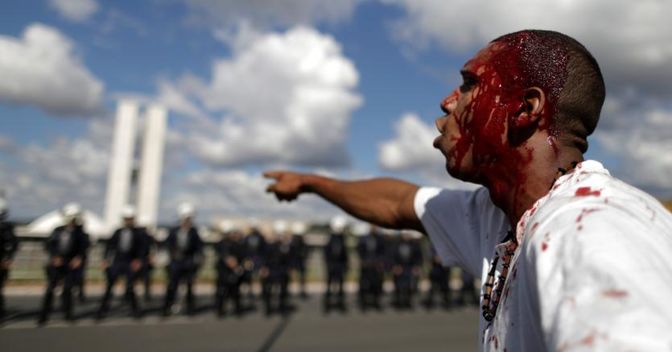 Manifestante ferito a Brasilia. Sullo sfondo le forze di polizia schierate (Reuters) 