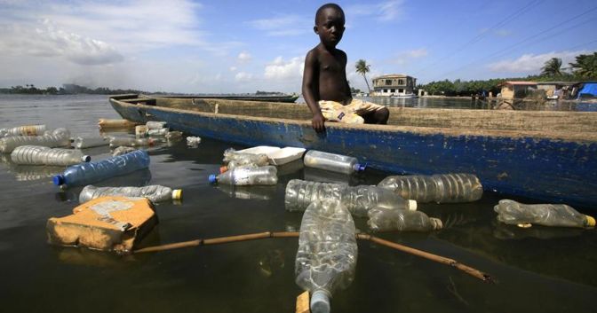 Un ragazzo della Costa d'Avorio esamina le bottiglie di plastica che galleggiano (Ansa) 