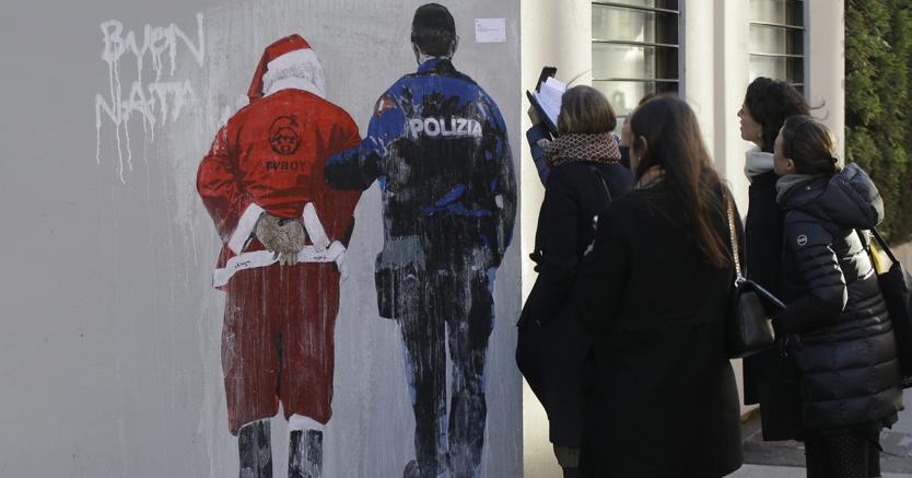 La gente guarda un murale dipinto dal pittore di pop art Tv Tvboy che mostra un agente di polizia che scorta un Babbo Natale ammanettato, a Milano. Il piccolo cartello in alto a destra recita: “Permesso di soggiorno negato per Babbo Natale” (Ap)