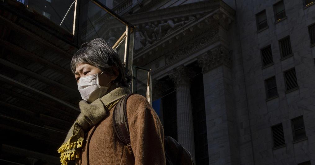 Una passante con mascherina davanti alla sede di Wall Street a New York (Epa) 