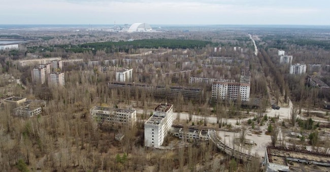 Pripyat, la città dei dipendenti della centrale. Oggi è inabitabile, la vegetazione si fa largo tra le case. Sullo sfondo l’arco che copre il reattore 