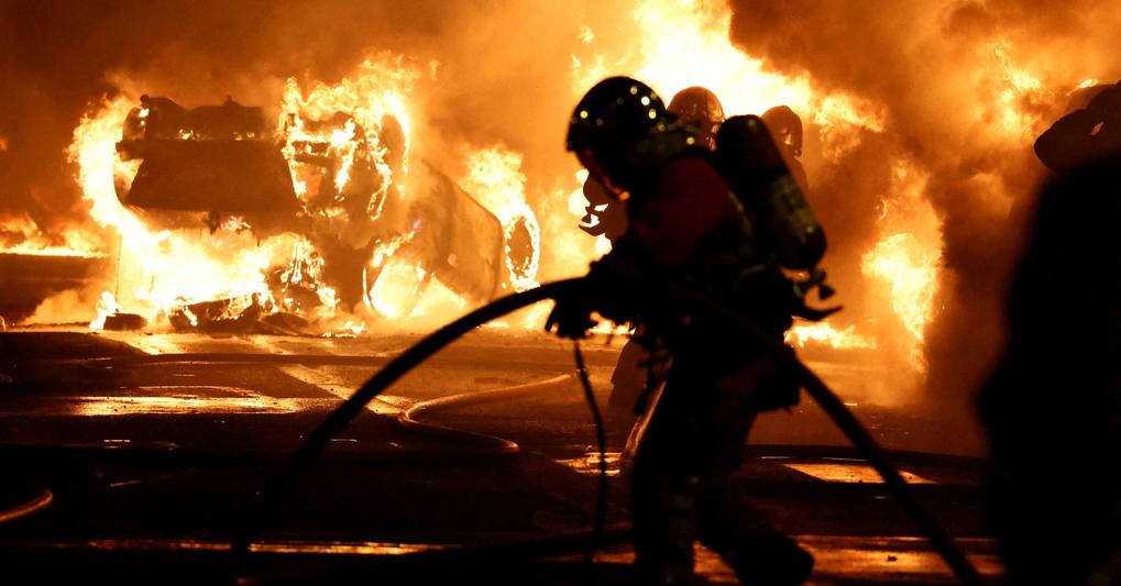 Vigili del fuoco lavorano per spegnere un’auto in fiamme a margine di una manifestazione a Nanterre, a ovest di Parigi (Reuters) 