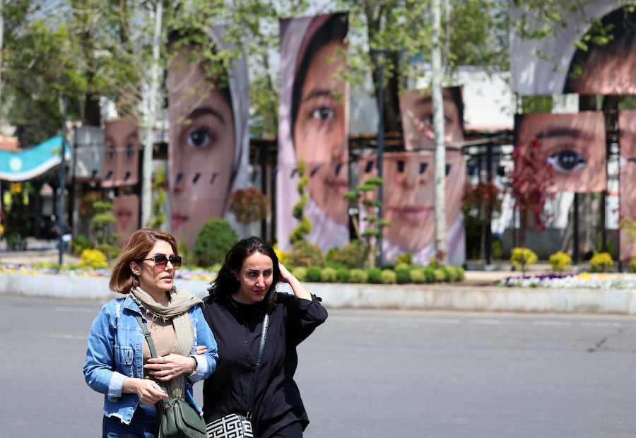 Donne iraniane camminano accanto ai ritratti di studentesse uccise in un attacco aereo a Minab, esposti in piazza Tajrish a Teheran (Epa)