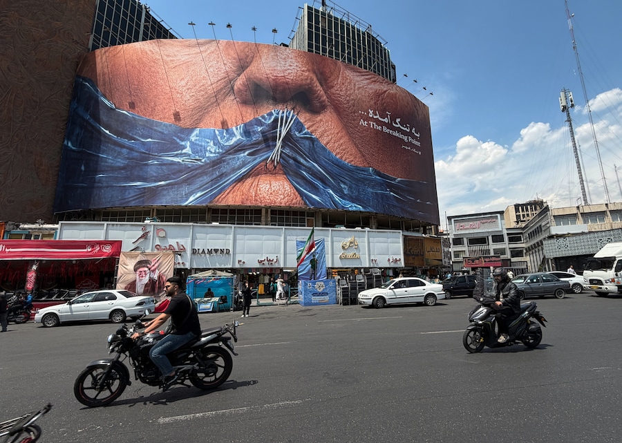 Sabato 2 maggio 2026, in una piazza del centro di Teheran, in Iran, alcune auto passano davanti a un cartellone pubblicitario su cui sono raffigurati lo Stretto di Hormuz e le labbra cucite del presidente degli Stati Uniti Donald Trump. (AP Photo/Vahid Salemi) (APN)