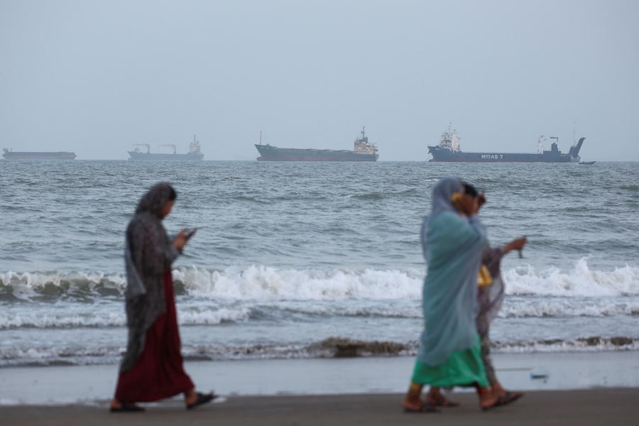 Alcune persone camminano mentre, vicino alla spiaggia di Bandar Abbas, in Iran, sono visibili delle navi nello Stretto di Ormuz, 26 agosto 2026. Majid Asgaripour/WANA (via REUTERS)