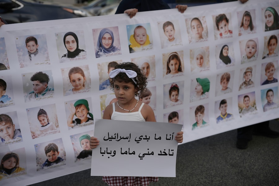 Una bambina tiene in mano un cartello su cui è scritto in arabo: “Non voglio che Israele mi porti via la mamma e il papà”, mentre si trova davanti a uno striscione che riproduce i ritratti di alcuni degli oltre 750 bambini libanesi uccisi dal 2024 nella guerra tra Israele e Hezbollah, durante una manifestazione a Beirut, in Libano (APN)