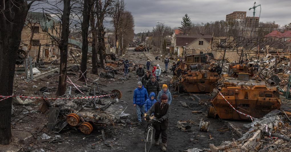 Residenti passano davanti a macchinari militari russi distrutti sulla strada, a Bucha (foto Ansa/Romano) 