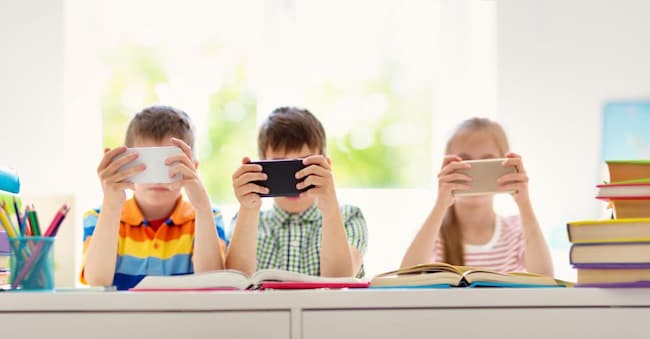 Children sitting in the room with smart phones. Pupils surfing at school