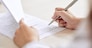 Crop shot of person with pen signing contract at desk in daylight