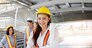 Portrait of Asian beautiful female engineer wearing safety helmet and uniform while standing in construction site with blur background of her colleagues
