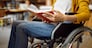 Disabled female student in wheelchair reading a book, disability, bookshelf and university library interior on background. Handicapped woman studying in college, paralyzed people get knowledge