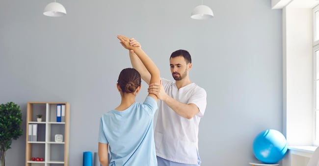 Young man doctor chiropractor or osteopath fixing woman patient arms joints during visit in manual therapy clinic interior. Professional chiropractor during work concept