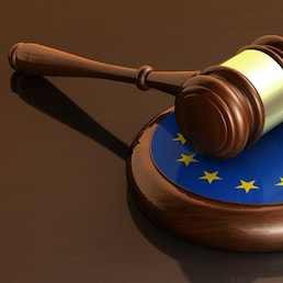 European Union laws, legal system and parliament concept with a 3d render of a gavel on a wooden desktop and the EU flag.