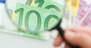 Hand holding a magnifying glass for better viewing of the banknotes