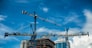 Cranes on modern skyscraper construction in city at sunny day with blue sky