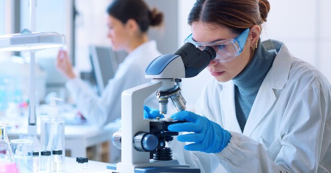 Young scientists conducting research investigations in a medical laboratory, a researcher in the foreground is using a microscope