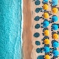 Aerial view of yellow and blue umbrellas on empty sandy beach, blue sea at sunset in summer. Tropical landscape with turquoise water. Travel and vacation in Sardinia, Italy. Top view from drone