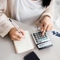 woman writing a list of debt on notebook calculating her expenses with calculator with many invoices , female hand doing accounting