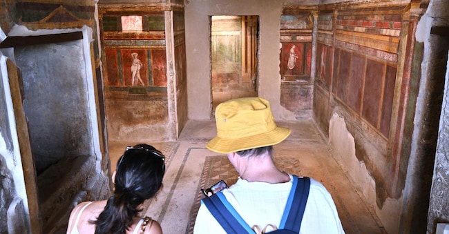 Tourists visit the 'Villa of Mysteries' lit by green energy as the roof has been partly retiled with innovative solar panels, on April 15, 2024 in Pompeii. The photovoltaic tiles look just like the ancient tiles of Pompeii but have solar cells inside, allowing the UNESCO World Heritage Site to preserve its aesthetics while generating clean energy to illuminate its frescoes. The project is in its early stages but experts say the tiles could one day play a part in helping historic centres across Italy turn green. The scheme weds emerging technologies with extraordinary murals unearthed in 1909 from under metres of volcanic ash at the Villa of the Mysteries, buried along with the rest of the city when Vesuvius erupted nearly 2,000 years ago. (Photo by Andreas SOLARO / AFP)