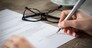Closeup shot of a woman signing a form. She's writing on a financial contract. Shallow depth of field with focus on tip of the pen.