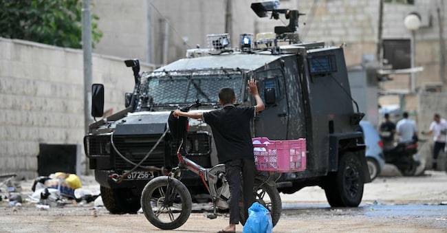 Un ragazzo palestinese alza il braccio in aria mentre i soldati israeliani ispezionano ciò che sta trasportando durante un raid a Jenin, nella Cisgiordania occupata, il 28 agosto 2024.(Photo by Ronaldo SCHEMIDT / AFP)