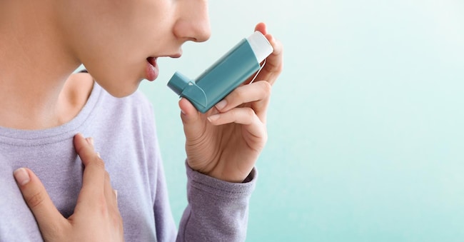 Young woman using inhaler against asthma on color background
