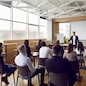 Team of people having class with business trainer. Group of male and female employees sitting at desks in modern office and listening to lecture by experienced teacher sharing knowledge and guidance