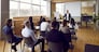 Team of people having class with business trainer. Group of male and female employees sitting at desks in modern office and listening to lecture by experienced teacher sharing knowledge and guidance