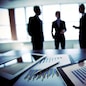 Close-shot of a tablet computer displaying financial data, three businessmen standing in the background