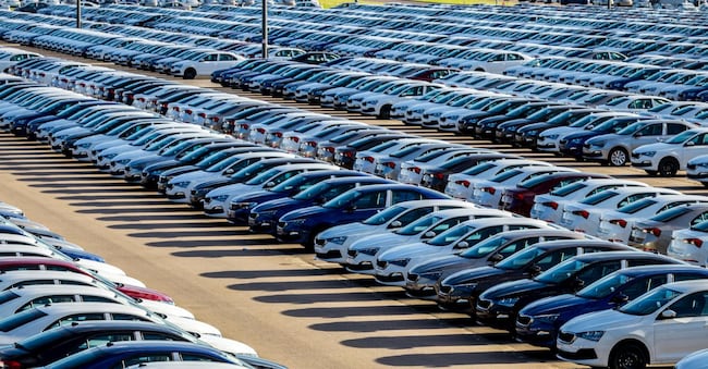 Rows of a new cars parked in a distribution center on a car factory on a sunny day. Top view to the parking in the open air.