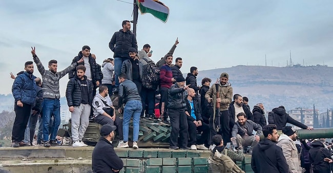 Un gruppo di manifestanti a bordi di un carro armato abbandonato a Umayyad Square, una piazza centrale della capitale siriana Damasco