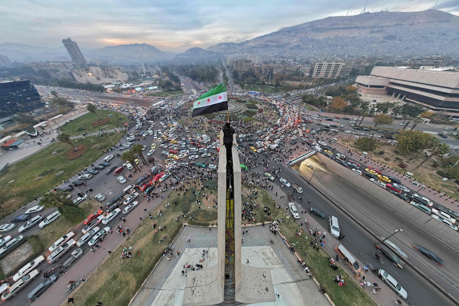 Una veduta aerea mostra un uomo siriano che sventola la bandiera siriana dell’era dell’indipendenza nella centrale piazza Umayyad di Damasco l’11 dicembre 2024. Il presidente deposto Bashar al-Assad è fuggito dalla Siria a seguito di un’offensiva fulminea guidata dall’islamista Hayat Tahrir al-Sham ( HTS) e i suoi alleati, che hanno posto fine in modo spettacolare a cinque decenni di brutale dominio del clan Assad. Photo by Bakr ALKASEM / AFP (AFP)