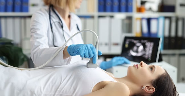 Doctor holds ultrasound probe on chest of patient in clinic closeup. Medical examination of breast in clinic