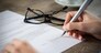 Closeup shot of a woman signing a form. She's writing on a financial contract. Shallow depth of field with focus on tip of the pen.