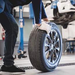 Male mechanic hold and rolling tire at repairing service garage background. Technician man replacing winter and summer tyre for safety road trip. Transportation and automotive maintenance concept