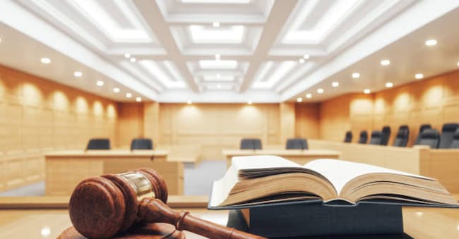 Interior of an empty courtroom with gavel, law books and sounding block on the desk.