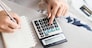 woman writing a list of debt on notebook calculating her expenses with calculator with many invoices , female hand doing accounting