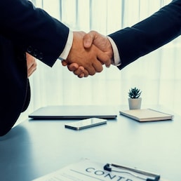 Two professionals successfully close business deal with closeup handshake, sealing the partnership agreement. Legal document and handshaking as formal agreement between two companies. Fervent