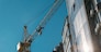 Building under construction and construction crane against blue sky and bright sun on summer day. Bottom view.