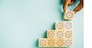 Close-up of a man's hand arranging wooden blocks in a stair-like formation, placing a cube with a target icon on top. Depicting growth, success, and strategic concepts. Isolated on a blue background.