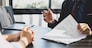 Businessman in suit in his office showing an insurance policy and pointing with a pen where the policyholder must to sign. Insurance agent presentation and consulting insurance detail to customer.