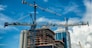 Cranes on modern skyscraper construction in city at sunny day with blue sky
