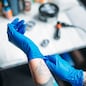 Female tattoo artist hands in blue sterile gloves, professional work tools on background. Tattooing in salon