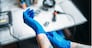 Female tattoo artist hands in blue sterile gloves, professional work tools on background. Tattooing in salon