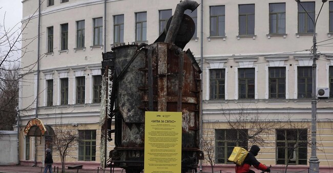 ? delivery courier rides his bike past damaged equipment retrieved from a Ukrainian power plant struck by Russian forces and put on display, in the Podil neighborhood of Kyiv on March 19, 2025, amid the Russian invasion of Ukraine. (Photo by Genya SAVILOV / AFP)
