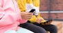 childhood, technology and people concept - close up of children with smartphone and tablet computer sitting on wooden street bench outdoors