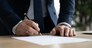 Close up young businessman standing near table with pen in hands, ready signing profitable offer agreement after checking contract terms of conditions, executive manager involved in legal paperwork.