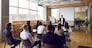 Team of people having class with business trainer. Group of male and female employees sitting at desks in modern office and listening to lecture by experienced teacher sharing knowledge and guidance