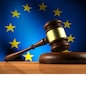 European Union law, legislation and parliament concept with a 3d rendering of a gavel on a wooden desktop and the EU flag on background.