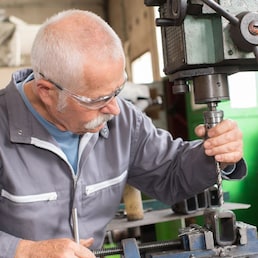 elderly worker watches processing of detail on milling machine